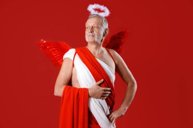 Kırmızı arka planda Aşk Tanrısı gibi giyinmiş olgun bir adam. Sevgililer Günü kutlaması