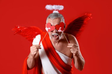 Aşk tanrısı gibi giyinmiş, kırmızı arka planda kalpleri olan olgun bir adam. Sevgililer Günü kutlaması