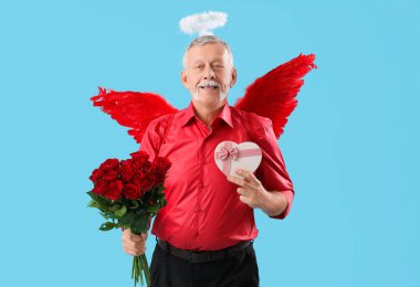 Aşk tanrısı gibi giyinmiş, gül ve mavi arka planda hediyeler taşıyan olgun bir adam. Sevgililer Günü kutlaması