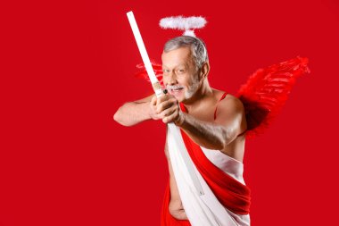 Aşk tanrısı gibi giyinmiş olgun bir adam kırmızı arka planda ok atıyor. Sevgililer Günü kutlaması