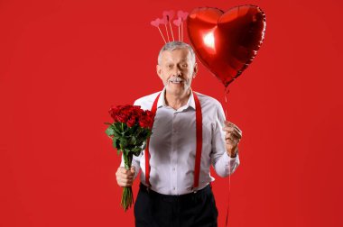 Aşk tanrısı gibi giyinmiş, balonlu ve kırmızı arka planda gülleri olan olgun bir adam. Sevgililer Günü kutlaması