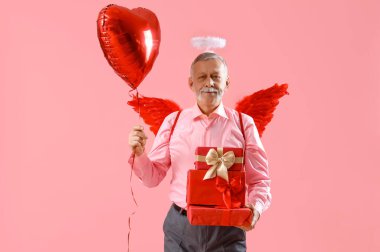 Aşk tanrısı gibi giyinmiş, balonlu ve pembe arka planda hediyeleri olan olgun bir adam. Sevgililer Günü kutlaması