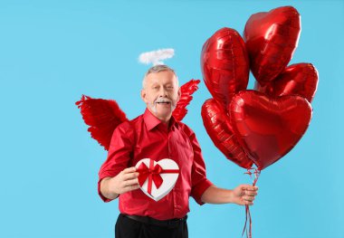 Aşk tanrısı gibi giyinmiş, balonlu ve mavi arkaplanlı olgun bir adam. Sevgililer Günü kutlaması