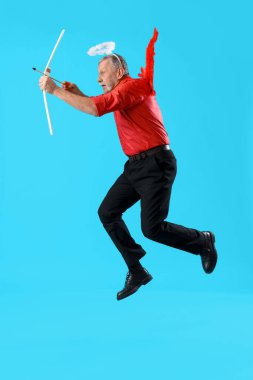 Aşk tanrısı gibi giyinmiş olgun bir adamın mavi arka planda ok atması. Sevgililer Günü kutlaması