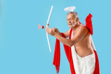 Aşk tanrısı gibi giyinmiş olgun bir adam mavi arka planda ok atıyor. Sevgililer Günü kutlaması