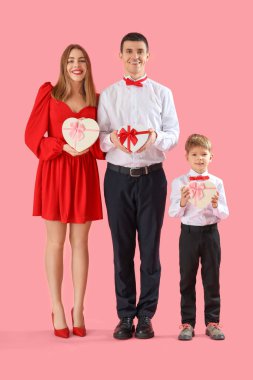 Ailesi ve pembe arka planda hediye kutuları olan küçük bir çocuk. Sevgililer Günü kutlaması