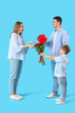 Küçük çocuk ve babası mavi arka planda hediyelerle annesini selamlıyorlar. Sevgililer Günü kutlaması