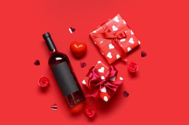 Kırmızı arka planda hediyeler ve dekor olan bir şişe şarap. Sevgililer Günü kutlaması