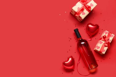 Kırmızı zemin üzerinde hediyeler, balonlar ve konfeti olan bir şişe şarap. Sevgililer Günü kutlaması