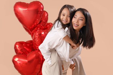 Genç Asyalı kadın ve kahverengi arka planda kalp şeklinde balonları olan küçük kızı. Sevgililer Günü kutlaması