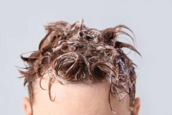 Young man with applied shampoo on his hair against light background