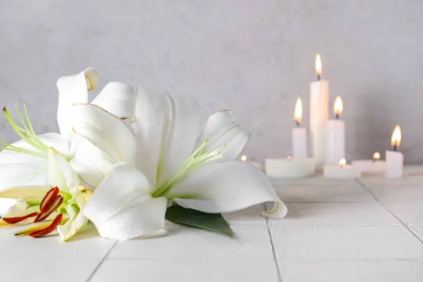 Beautiful lily flowers with burning candles on table