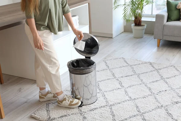 Mutfakta ayak pedalı olan bir kadın kullanılmış mendili çöp kutusuna atıyor.