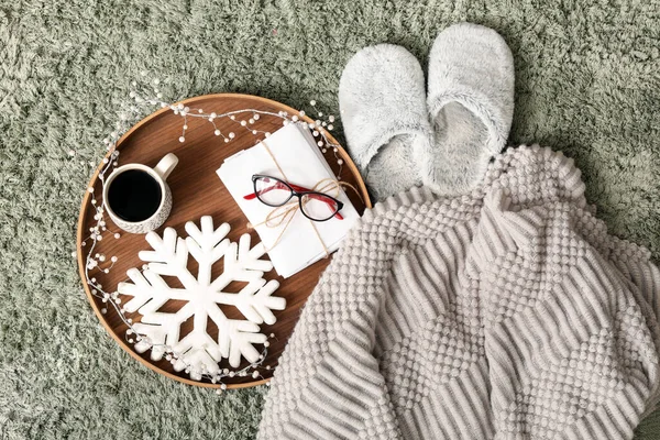 Soft slippers with plaid, coffee cup, letters and Christmas decor on green carpet, top view