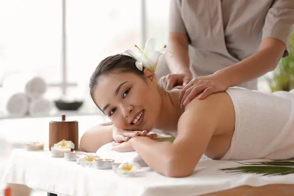 Young Asian woman with flower getting massage in spa salon, closeup