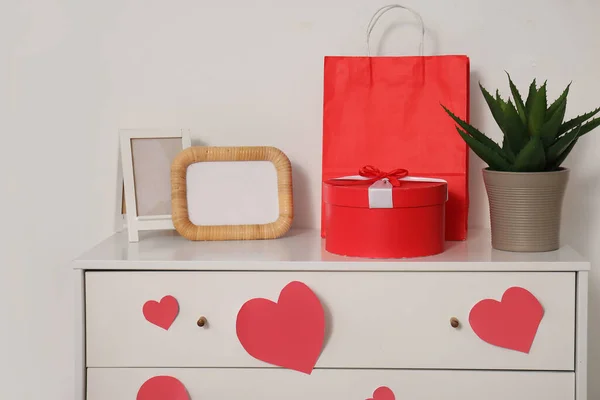 Chest of drawers with gift box, blank frame and paper hearts. Valentine\'s Day celebration