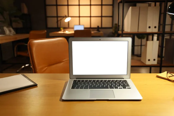 Blank laptop on table in office at night, closeup