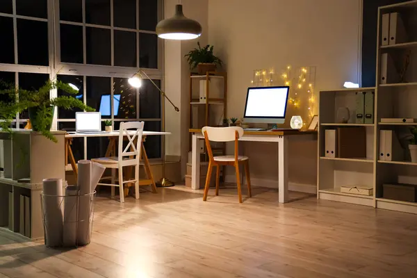 Interior of office with desks and glowing lamps at night