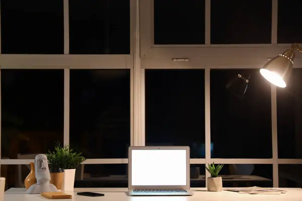 Blank laptop and plants on desk in office at night