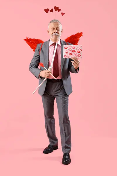 Mature man dressed as Cupid holding letter with lipstick kiss marks and bow on pink background. Valentine\'s Day celebration