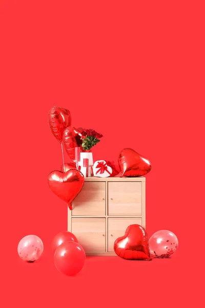 Wooden chest of drawers with heart-shaped air balloons and gifts on red background. Valentine\'s day celebration