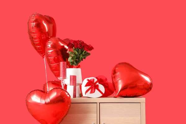 Wooden chest of drawers with heart-shaped air balloons, roses, candles and gifts on red background. Valentine\'s day celebration
