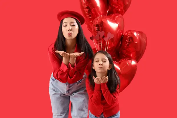 年轻的亚洲女人和她的小女儿 戴着心形的气球 在红色的背景下亲吻着 — 图库照片