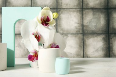 Dekoratif alçı podyumlar ve güzel orkide çiçekleri gri kiremitli duvarın yanındaki beyaz masada.