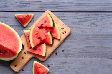 Tahtada taze karpuz parçaları ve mavi ahşap arka planda tohumlar var.