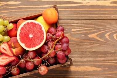 Tahta arka planda farklı taze meyvelerle dolu bir kutu.