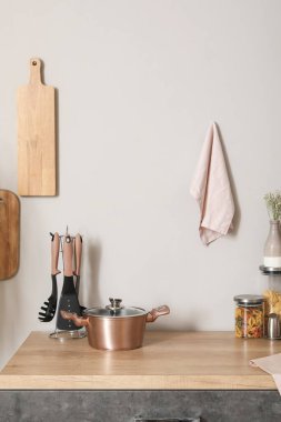 Ahşap mutfak tezgahı, yemek tenceresi, mutfak aletleri ve beyaz duvarda asılı tahta kesme tahtaları.