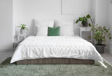 Yatak odasının içinde beyaz battaniyeli ve yastıklı rahat bir yatak.