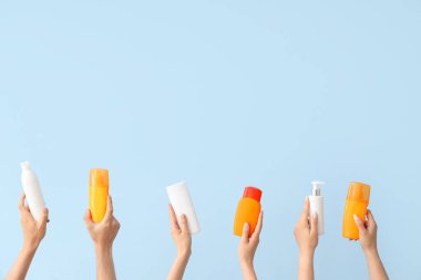 Mavi arka planda güneş kremi şişeleri olan kadın elleri