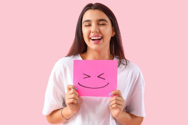 Pembe arka planda kağıt gülüşü olan genç bir kadın.