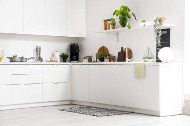 Modern mutfağın içinde lavabo, ev bitkileri ve çatal bıçaklarla dolu beyaz tezgahlar.