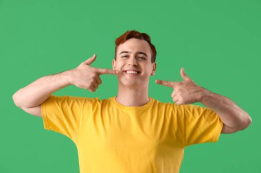 Yeşil arka planda dişlerini gösteren genç adam, yakın plan.