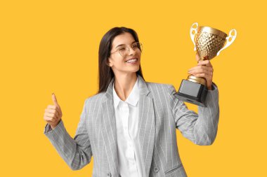 Sarı arka planda altın bardaklı genç bir iş kadını.