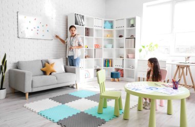 Asyalı kadın konuşma terapisti küçük kıza ofiste harfleri nasıl telaffuz edeceğini öğretiyor.