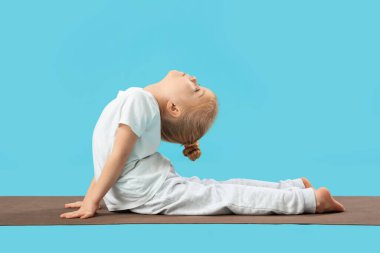 Mavi arka planda minder üzerinde yoga yapan sevimli küçük kız.