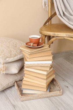 Çay fincanı kitap yığını ve bej duvarın yanındaki yastık yığını