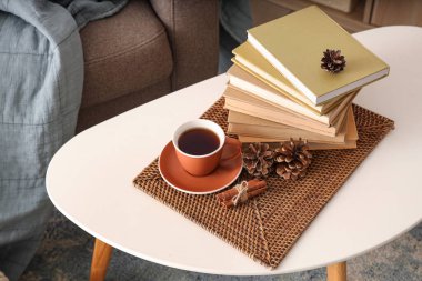 Oturma odasında bir fincan sıcak çay, kozalak ve kitap olan sehpa, yakın plan.