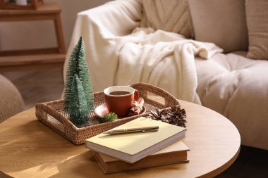 Kitaplı ahşap sehpa, mini Noel ağaçları ve aydınlık oturma odasının içinde bir fincan çay.