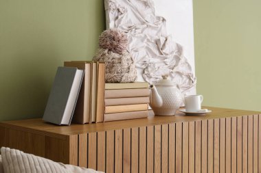 Kitaplar, çaydanlık ve fincanlar yeşil duvarın yanındaki ahşap dolapta, yakın plan.