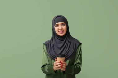 Yeşil arka planda bir fincan sıcak kahveyle tesettürlü güzel Müslüman kadın.