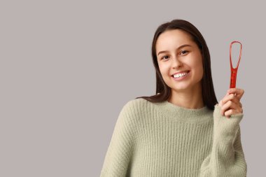 Gri arka planda dil kazıyıcısı olan güzel genç bir kadın.