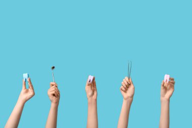 Mavi arka planda diş modelleri ve diş aletleri olan kadın elleri