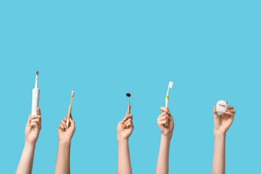 Diş fırçası, diş ipi ve mavi arka planda ayna olan kadın elleri.