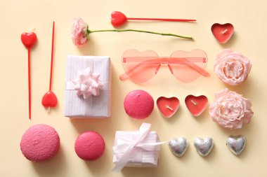 Pembe kalp şeklinde güneş gözlüğü, tatlı, hediye ve sarı arka planda dekor. Sevgililer Günü konsepti