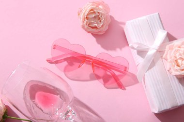 Pembe kalp şeklinde güneş gözlüğü hediye kutusu, cam ve gül rengi arka planda. Sevgililer Günü konsepti