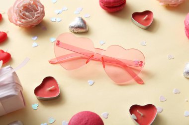 Sarı arka planda şekerli, mumlu ve dekorlu pembe kalp şeklinde güneş gözlüğü. Sevgililer Günü konsepti